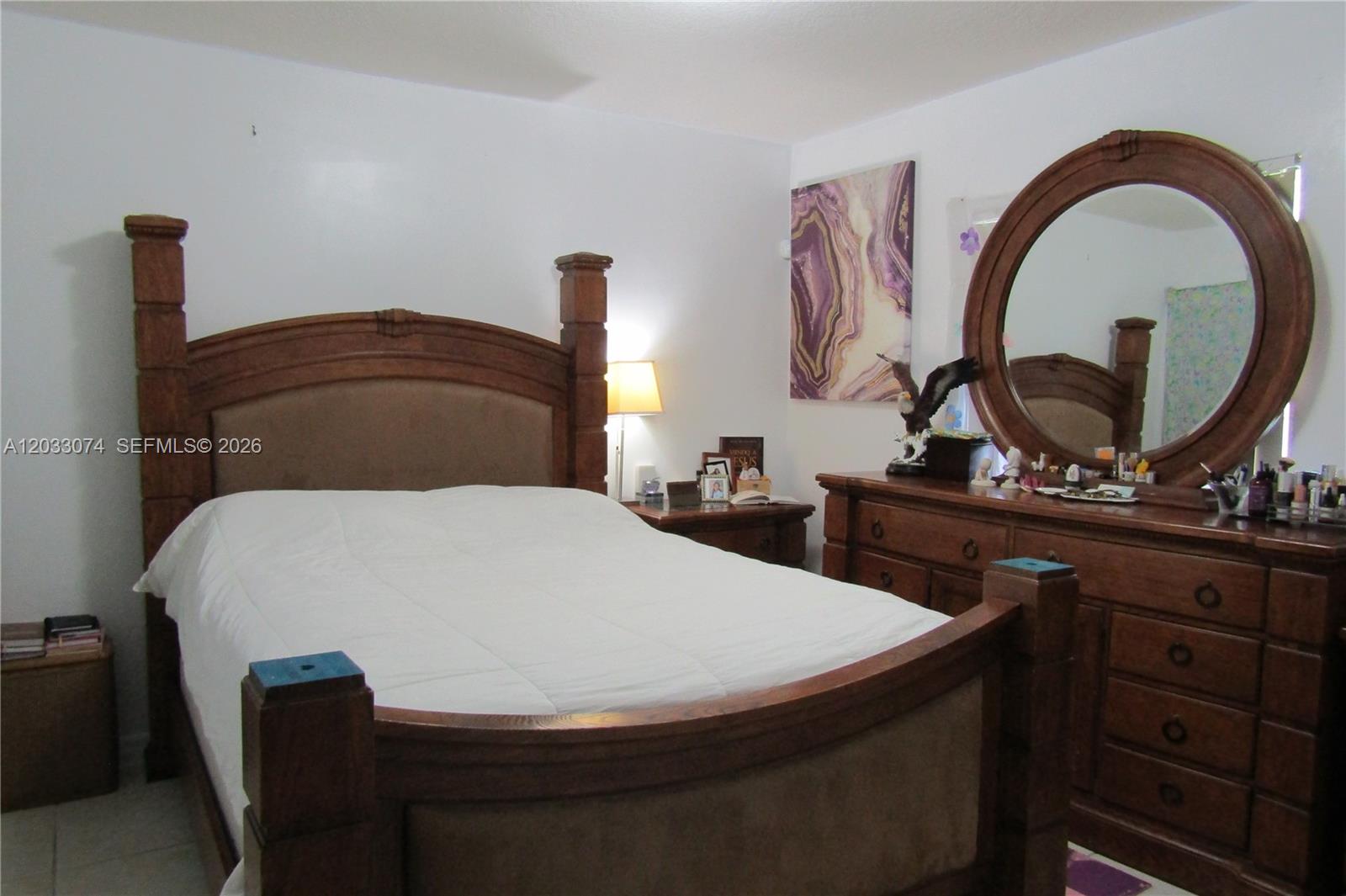 A bedroom features a wooden bed frame, a matching dresser with a round mirror, and artwork — 942 SW 8th Pl, Florida City FL 33034, FLORIDA CITY, FL