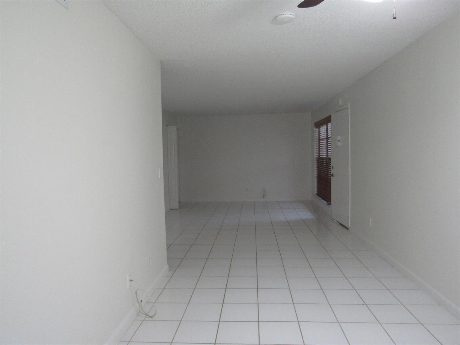 An empty room with white walls, white tile flooring, and a door with blinds — 2110 SE Edler Drive, Stuart FL 34994, STUART, FL
