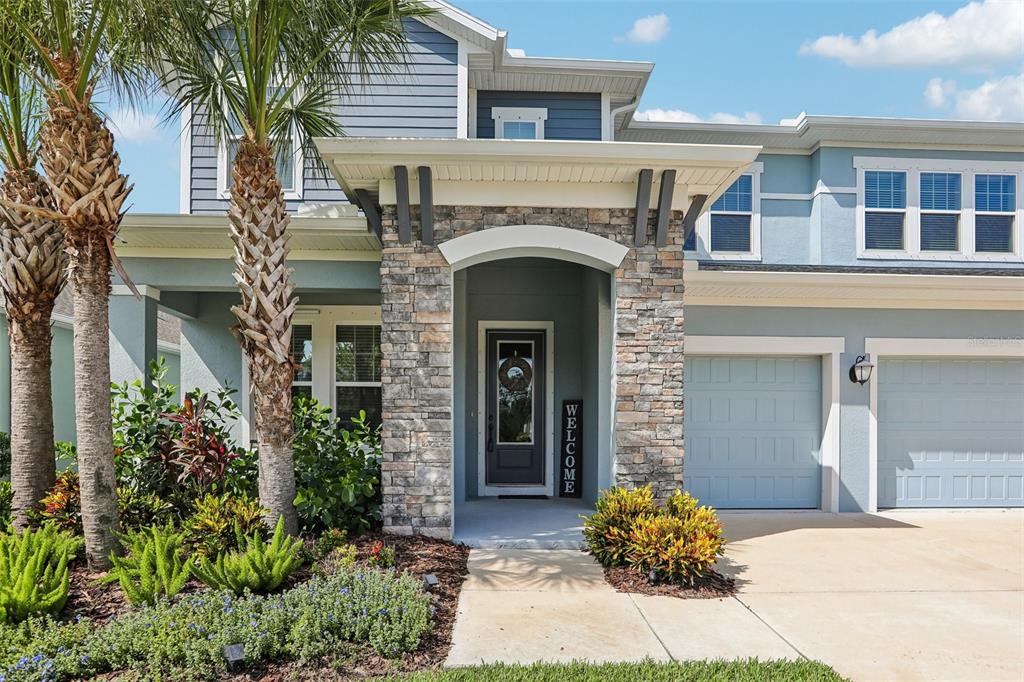 A grassy backyard features a row of trees, hedges, and a view of distant woods — 3275 TOUR TRACE, LAND O LAKES, FL