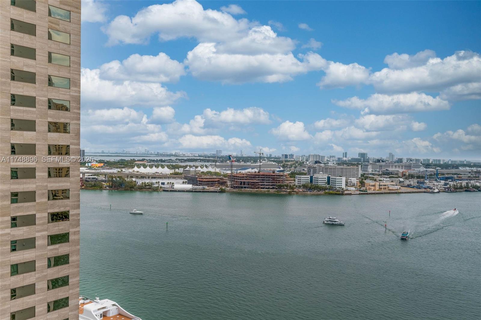 An exterior view shows a high-rise building facade overlooking a bay with boats and construction — 335 S Biscayne Blvd # 2402, Miami FL 33131, MIAMI, FL