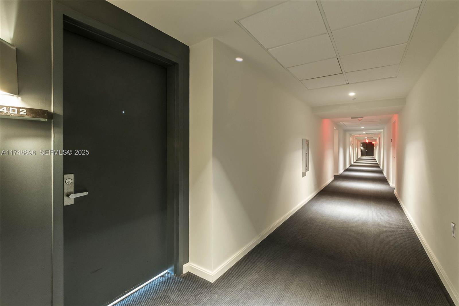 A long, carpeted hallway in a building features a dark door labeled 402 — 335 S Biscayne Blvd # 2402, Miami FL 33131, MIAMI, FL
