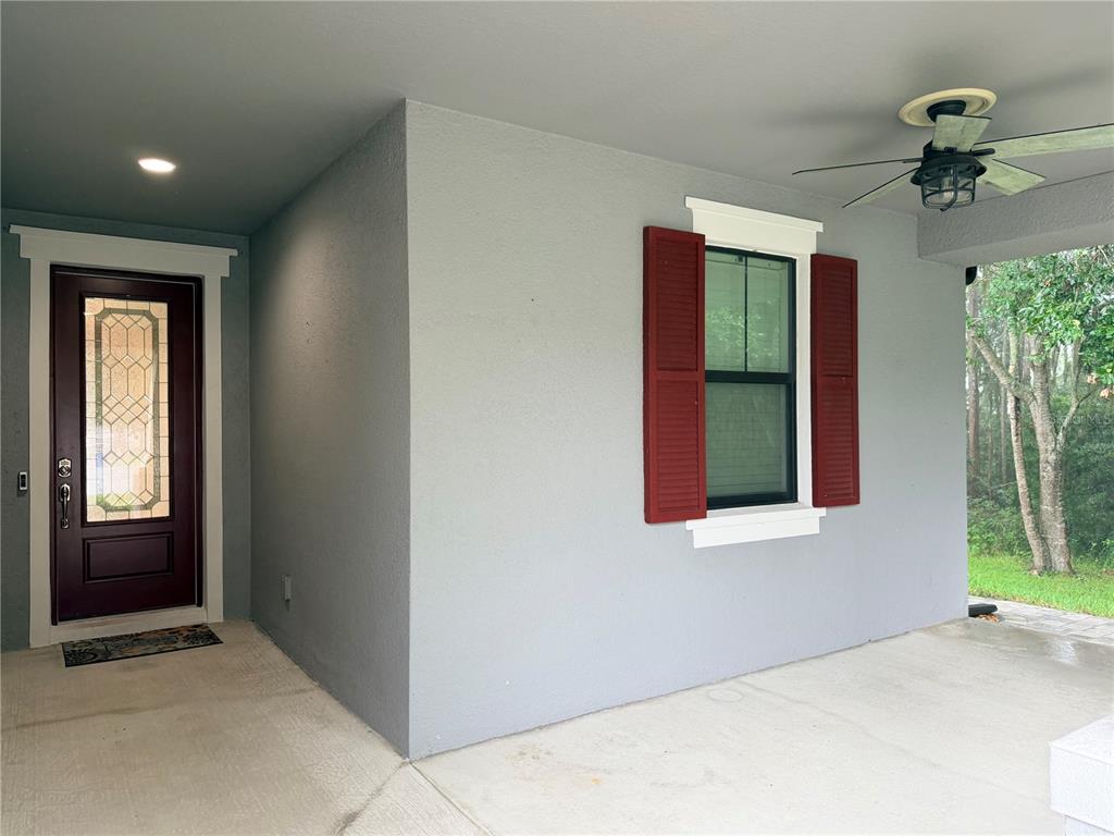 A covered front porch features white tapered columns, gray siding, and a small flamingo garden flag — 8429 AUBURN RISE COURT, LAND O LAKES, FL