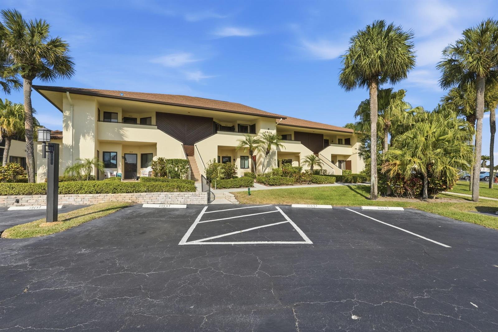 A two-story apartment building with a parking lot and palm trees in the foreground — 6901 SE Constitution Boulevard # 102, Hobe Sound FL 33455, HOBE SOUND, FL