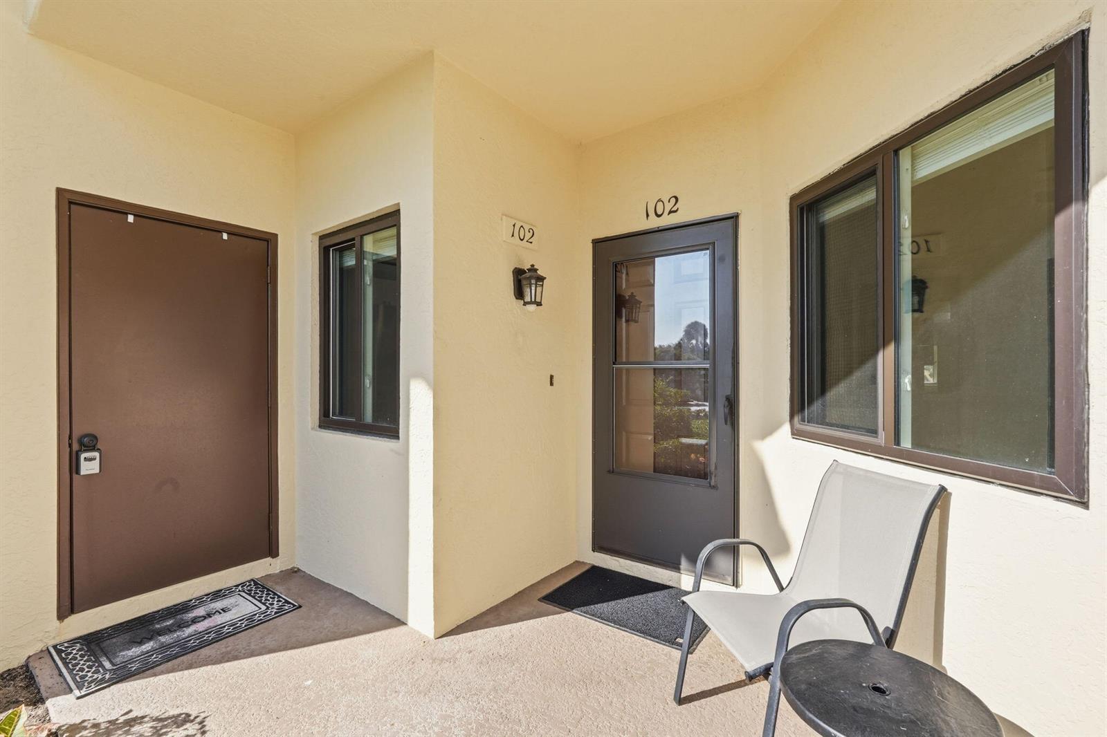 An exterior view of a building entrance with two brown doors, windows, and a chair — 6901 SE Constitution Boulevard # 102, Hobe Sound FL 33455, HOBE SOUND, FL