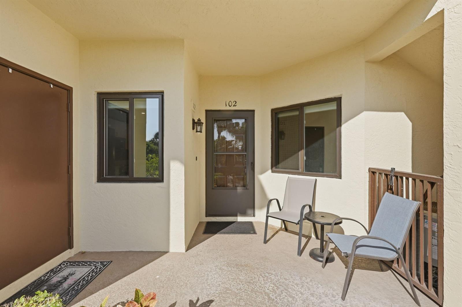 A covered patio entrance features a front door numbered 102, two chairs, and a table — 6901 SE Constitution Boulevard # 102, Hobe Sound FL 33455, HOBE SOUND, FL
