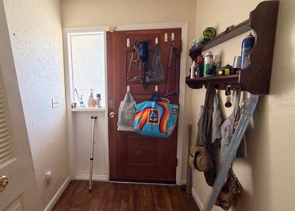 A wooden front door with hanging bags and a wall-mounted shelf in a small entryway — 8822 E CRESCO LANE, INVERNESS, FL