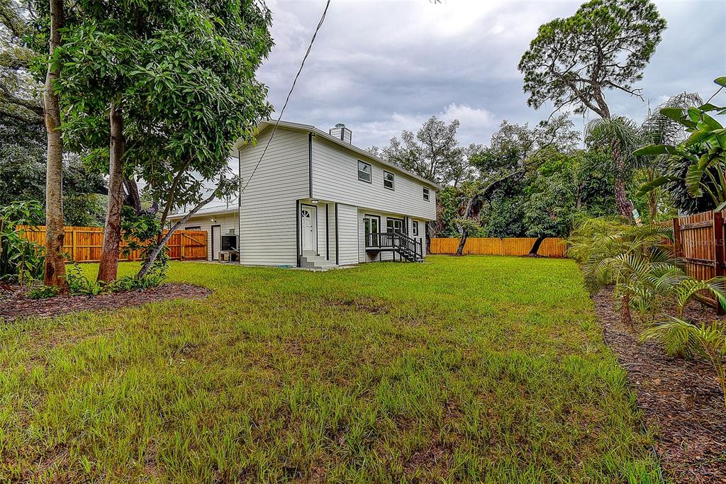 A two-story house with light-colored siding stands in a large, grassy backyard with wooden fencing — 5546 113TH STREET, SEMINOLE, FL