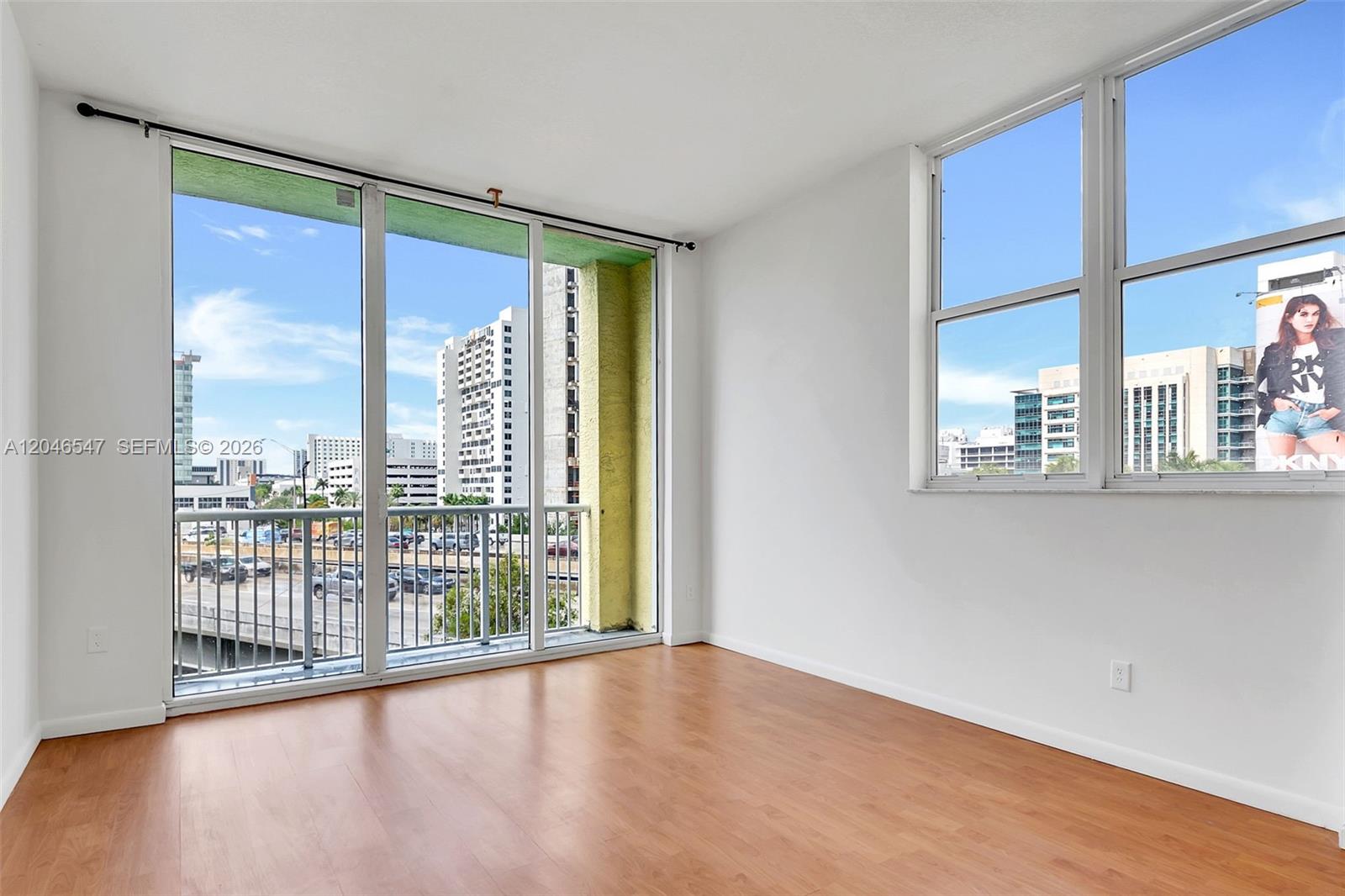 An empty room with wood-look flooring, large windows, and a balcony overlooking a city street — 1350 NW 8th Ct # 5, Miami FL 33136, MIAMI, FL