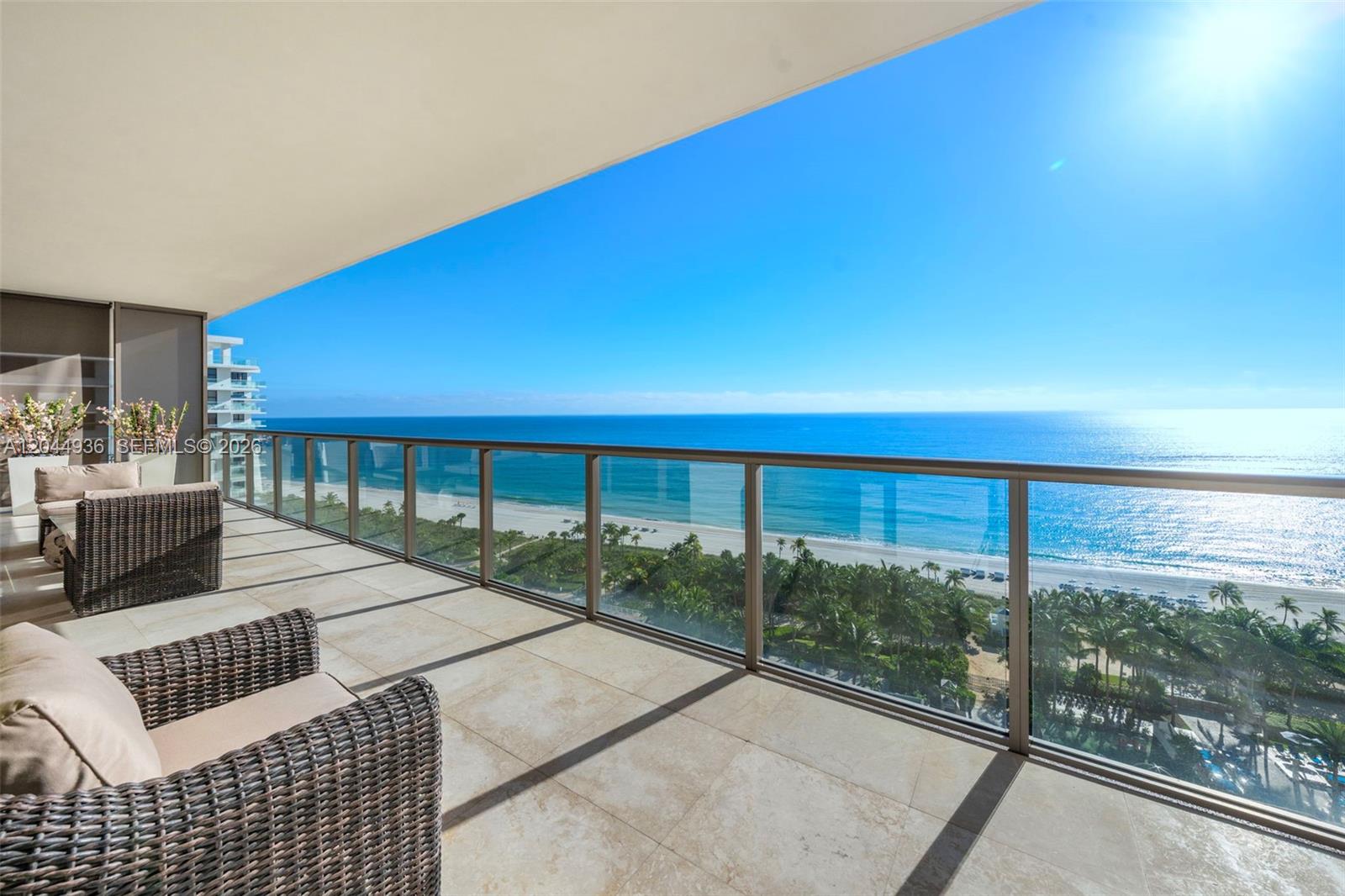 A balcony with wicker furniture overlooks the ocean, beach, and palm trees — 9705 Collins Ave # 1402N, Bal Harbour FL 33154, BAL HARBOUR, FL