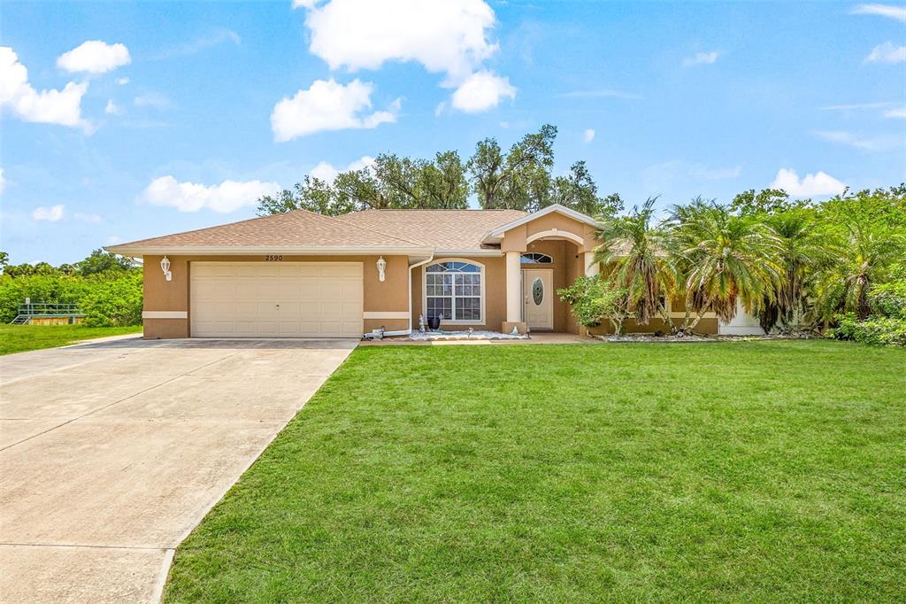 A single-story tan house with a two-car garage and a large front lawn — 2590 ABBOTSFORD STREET, NORTH PORT, FL