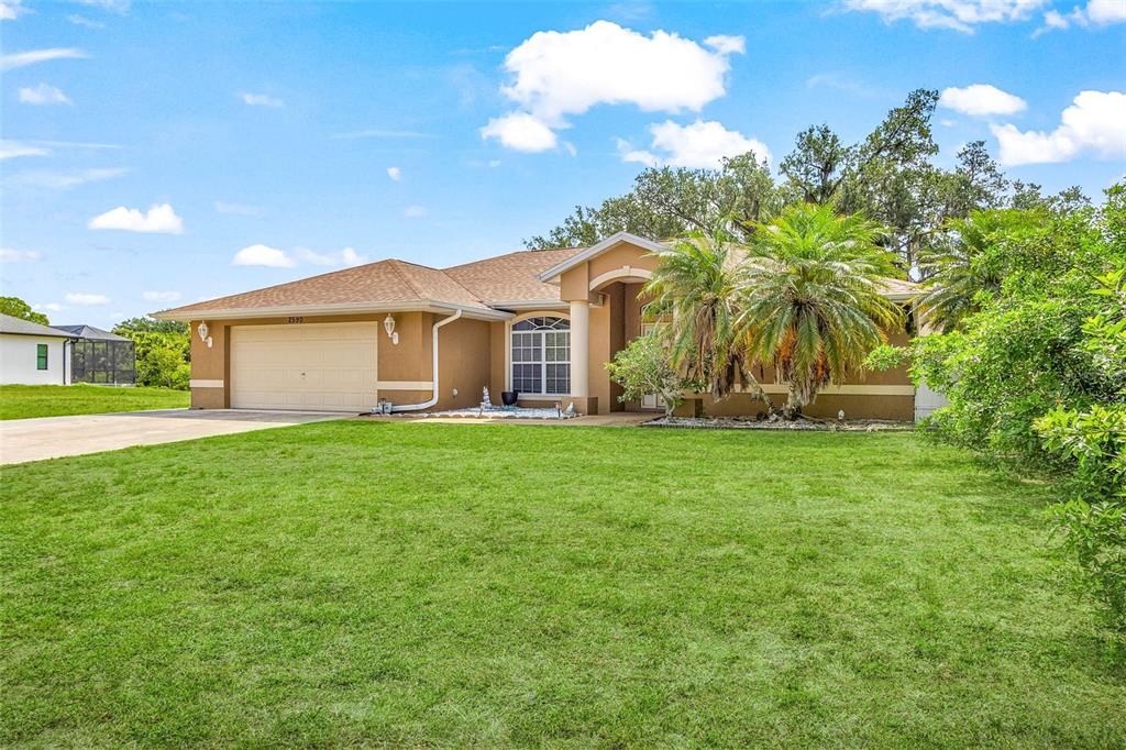 A tan, single-story suburban house with a two-car garage and palm trees in the front — 2590 ABBOTSFORD STREET, NORTH PORT, FL