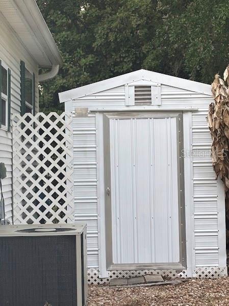 A white metal storage shed stands next to a house with a lattice privacy screen — 25155 NE 142ND LANE UNIT 212, FORT MC COY, FL