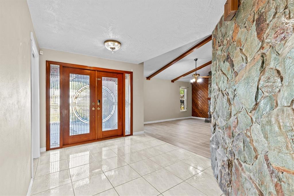 A tiled entryway features double wooden doors with decorative glass and a stone accent wall — 3149 CARLOS DRIVE, DUNEDIN, FL