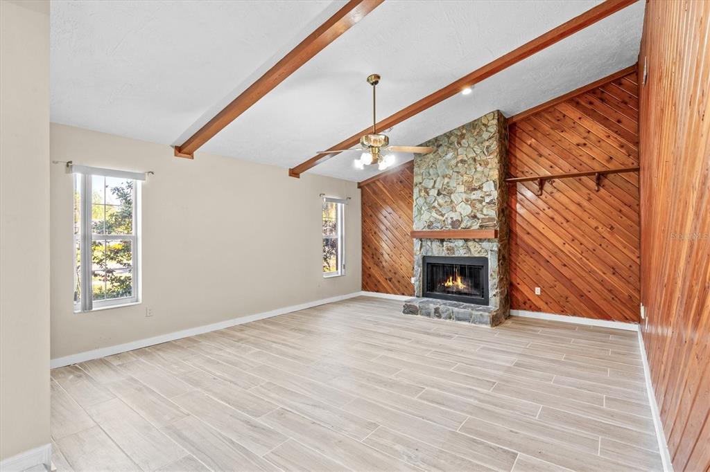 A living room features wood-paneled walls, a stone fireplace, vaulted ceilings with beams, and tile flooring — 3149 CARLOS DRIVE, DUNEDIN, FL