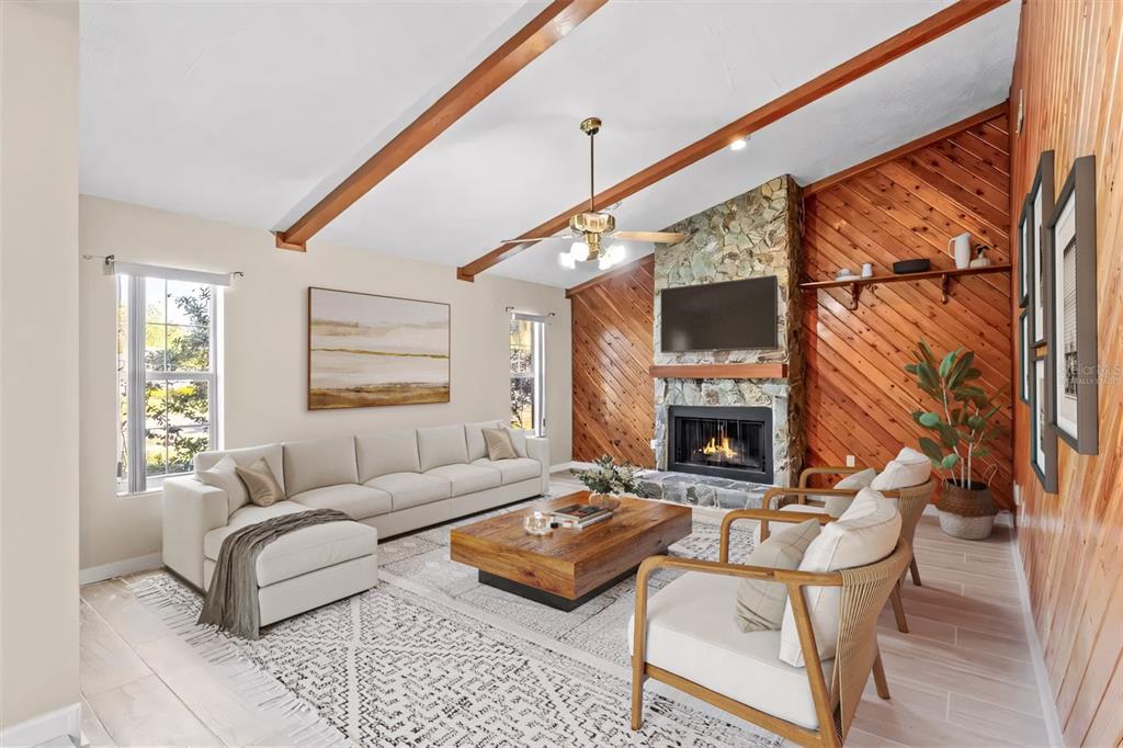 A living room features a stone fireplace, wood-paneled walls, exposed ceiling beams, and neutral furniture — 3149 CARLOS DRIVE, DUNEDIN, FL