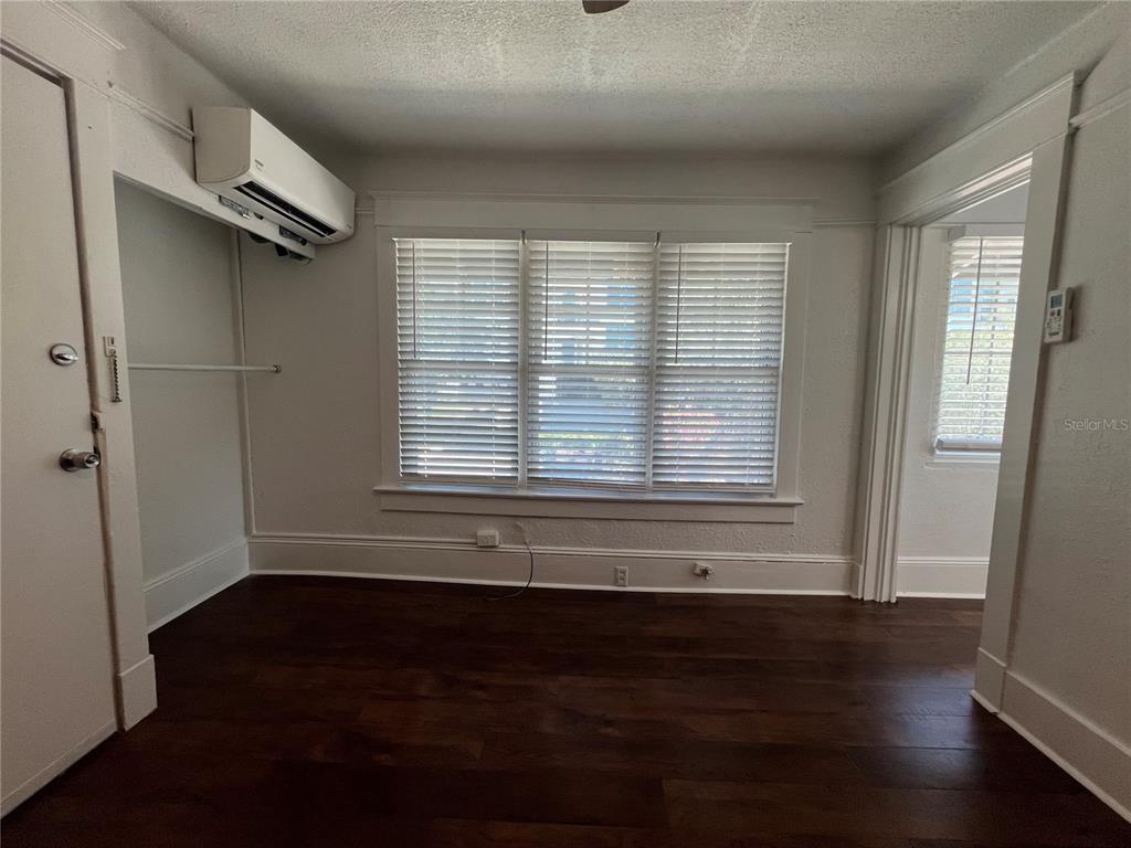 A room with dark wood flooring, white walls, a mini-split unit, and three windows — 510 E JACKSON ST UNIT 7, ORLANDO, FL