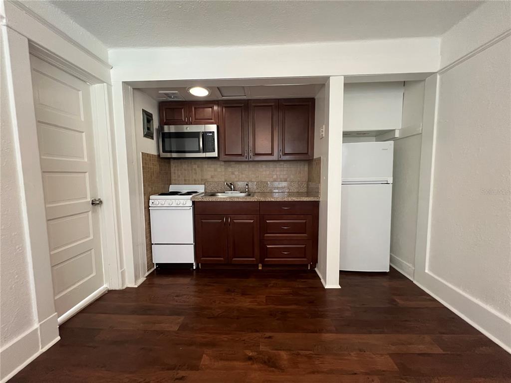 A small kitchen features dark wood cabinets, a white stove, and a white refrigerator — 510 E JACKSON ST UNIT 7, ORLANDO, FL