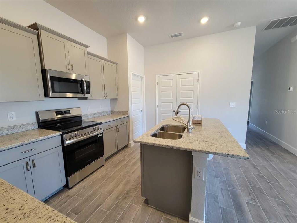 A kitchen features gray cabinets, granite countertops, a stainless steel oven, and a center island — 4457 SW 91ST LANE ROAD, OCALA, FL