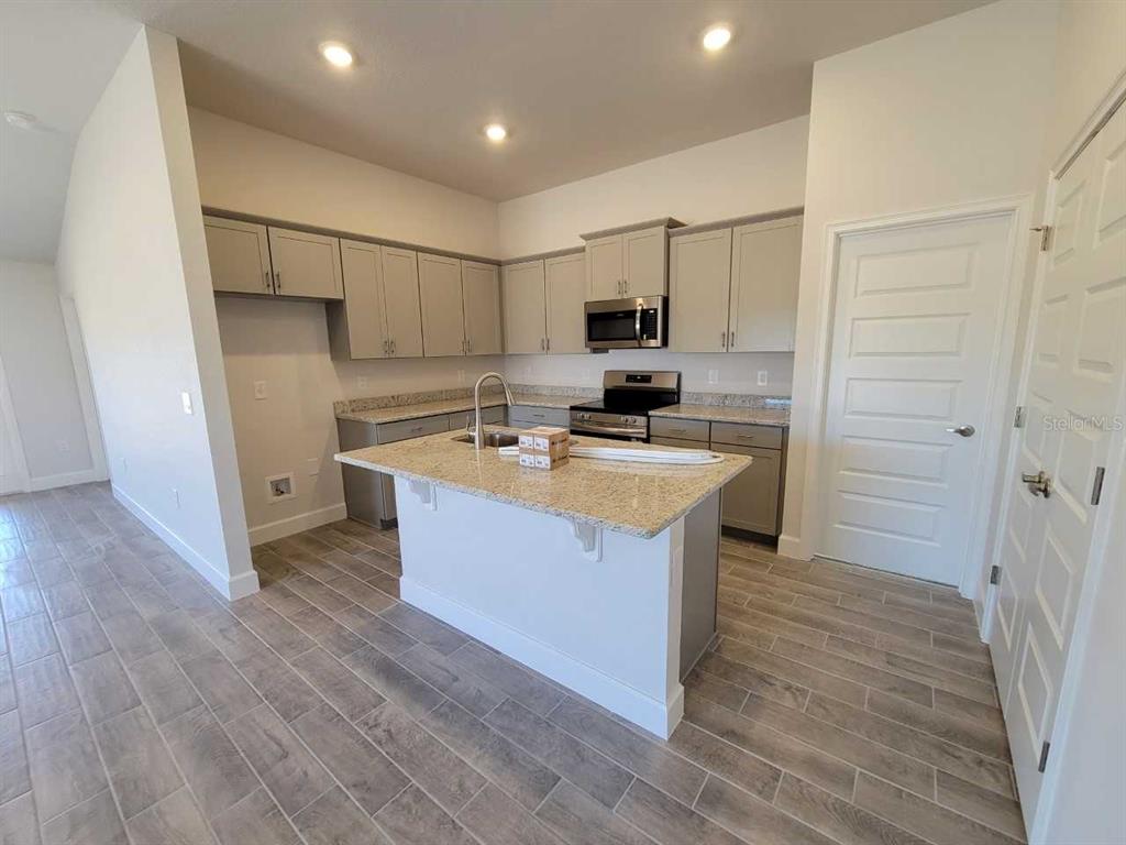 A kitchen features light gray cabinets, granite countertops, a center island, and wood-look tile flooring — 4457 SW 91ST LANE ROAD, OCALA, FL