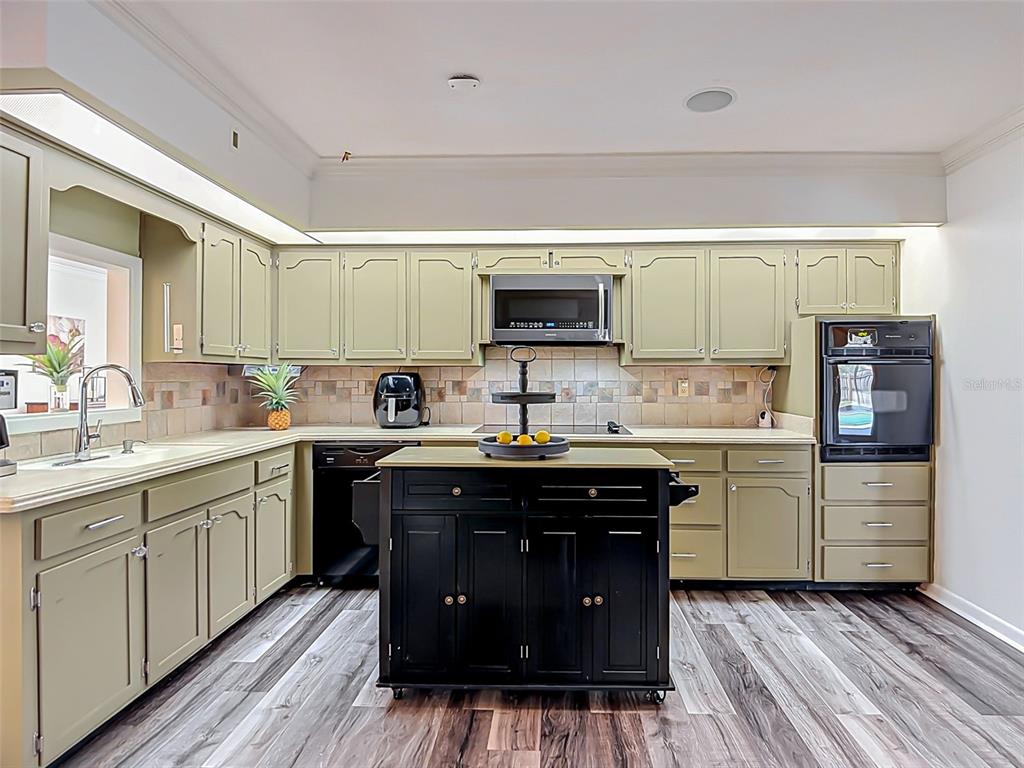A kitchen features sage green cabinets, a black rolling island, and wood-look flooring — 1231 NEWPORT AVENUE, LAKELAND, FL