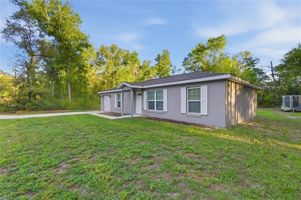 A single-story gray house with white shutters and a concrete driveway sits on a grassy lot — 15541 NE 13TH LANE, WILLISTON, FL
