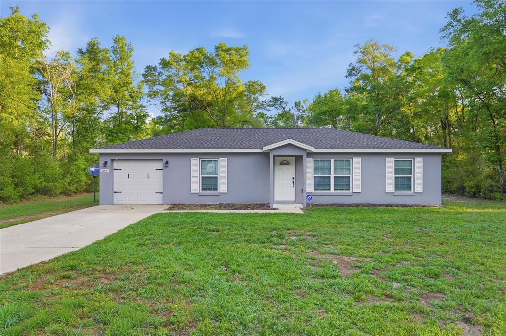 A single-story gray house with a one-car garage and white shutters sits on a lawn — 15541 NE 13TH LANE, WILLISTON, FL