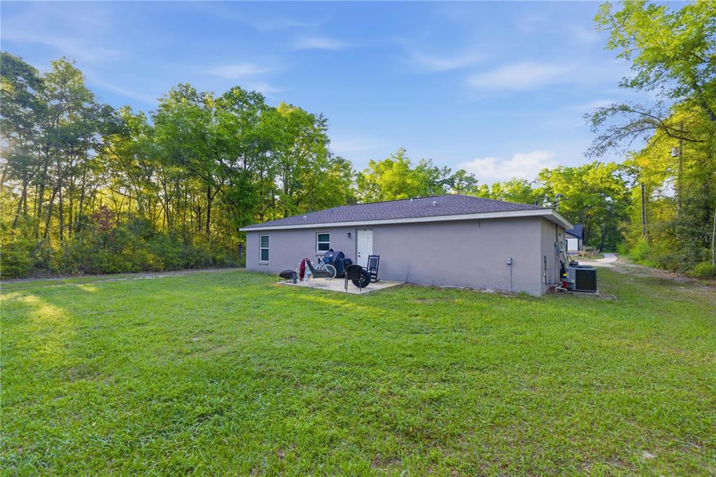 The rear exterior of a gray, single-story house features a small concrete patio and lawn — 15541 NE 13TH LANE, WILLISTON, FL