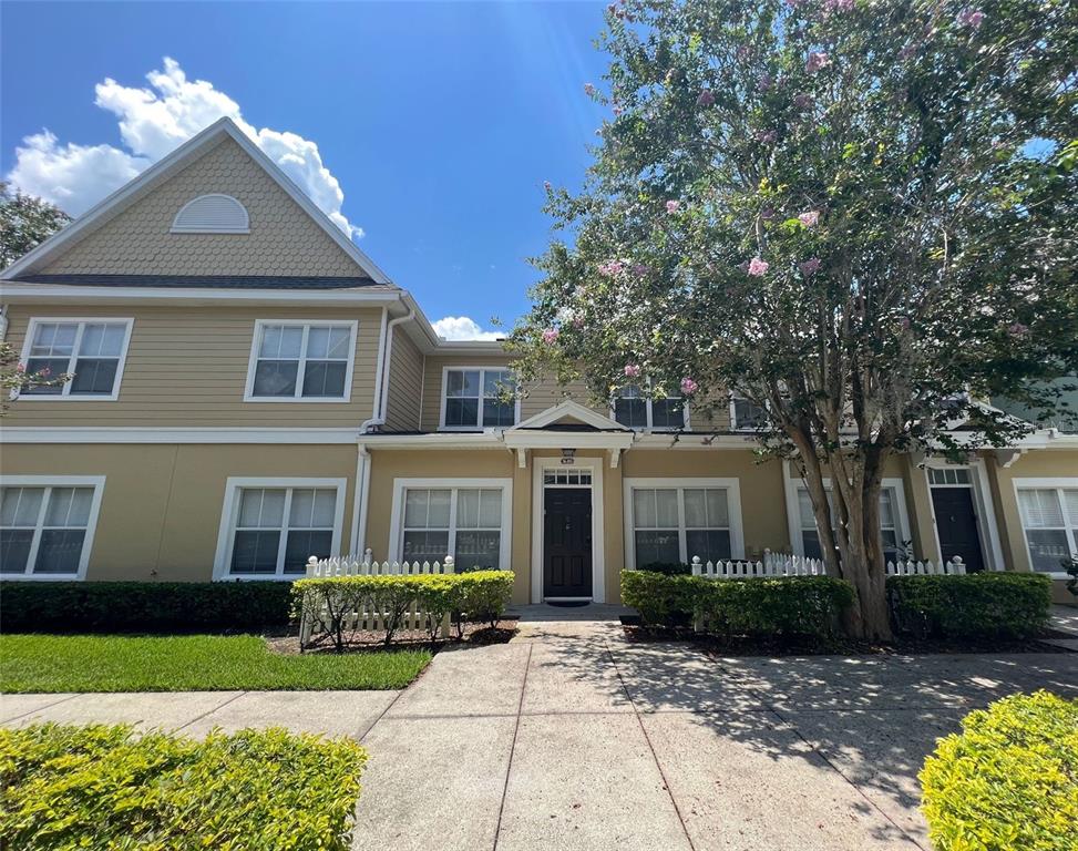 A two-story tan townhouse with a white picket fence and a large flowering tree — 2220 SAN VITTORINO CIRCLE UNIT 105, KISSIMMEE, FL