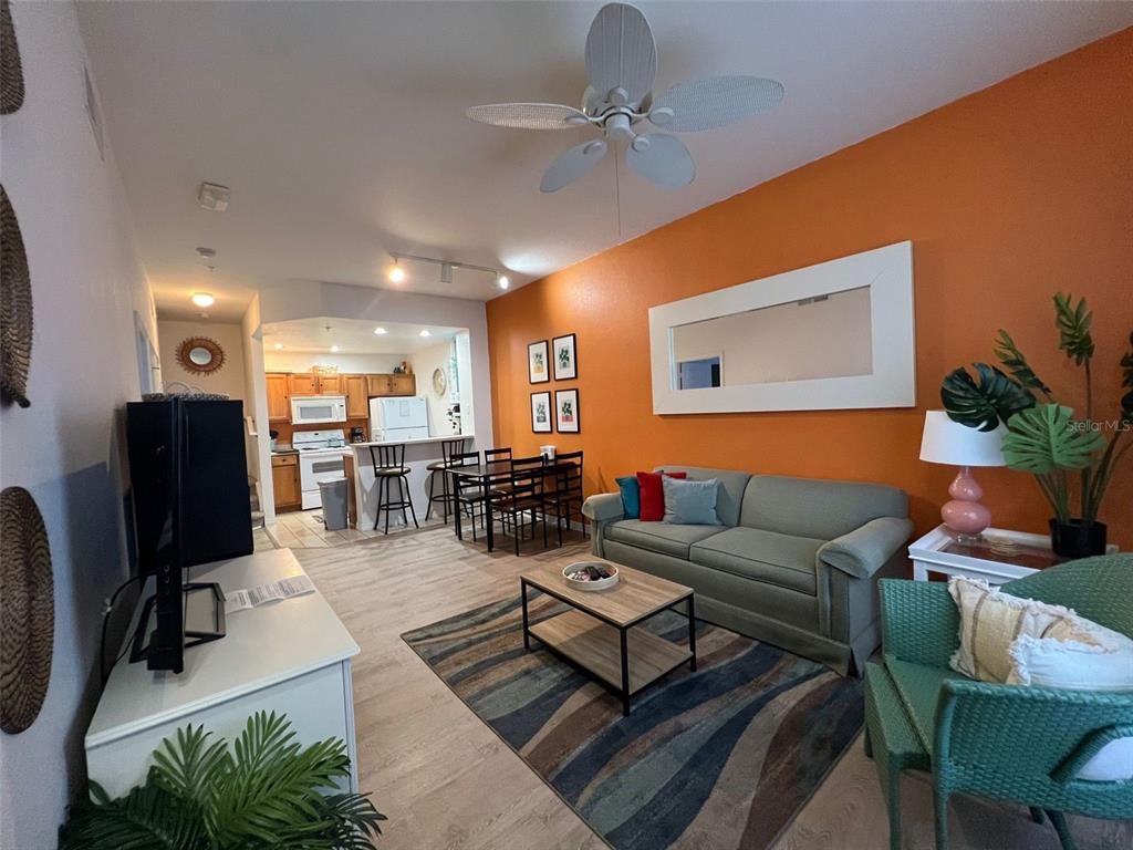 A living room with an orange accent wall, a green sofa, and an open kitchen — 2220 SAN VITTORINO CIRCLE UNIT 105, KISSIMMEE, FL