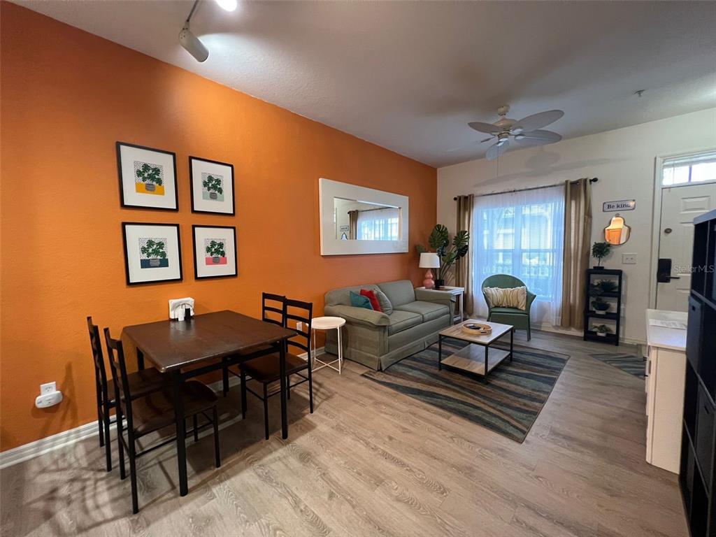 A living and dining room area features an orange accent wall, wood-look flooring, and furniture — 2220 SAN VITTORINO CIRCLE UNIT 105, KISSIMMEE, FL