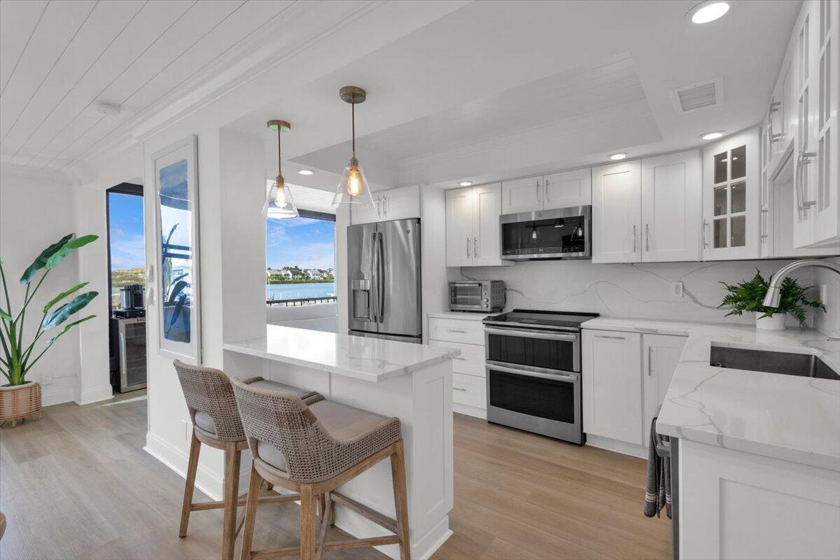 A bright kitchen features white cabinetry, stainless steel appliances, a marble island, and water views — 1648 Jupiter Cove Drive # 210, Jupiter FL 33469, JUPITER, FL