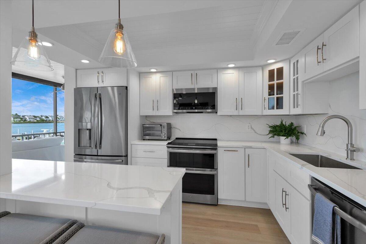 A modern white kitchen features stainless steel appliances, quartz countertops, and a view of water — 1648 Jupiter Cove Drive # 210, Jupiter FL 33469, JUPITER, FL