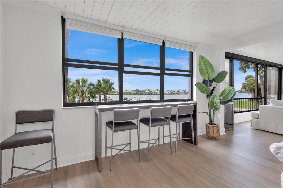 A room with light wood flooring features a bar table with three stools facing windows — 1648 Jupiter Cove Drive # 210, Jupiter FL 33469, JUPITER, FL