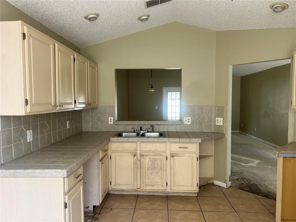A kitchen with tile countertops, light-colored cabinets, and a pass-through window to another room — 1982 GREYSTONE TRAIL, ORLANDO, FL