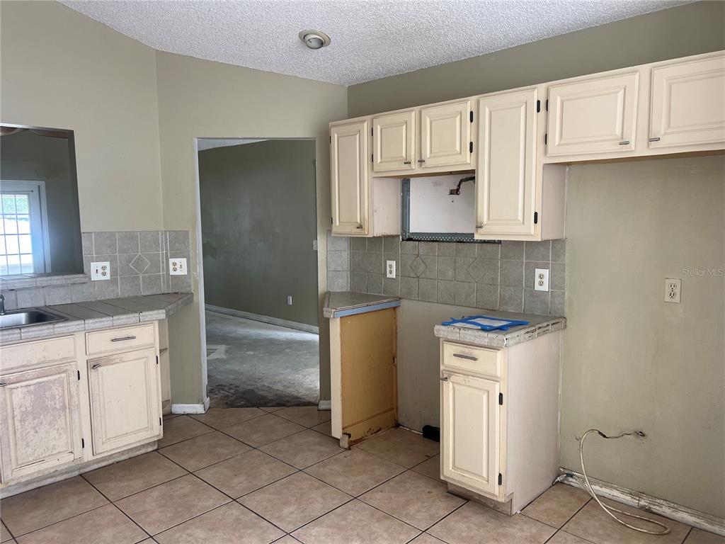 An unfinished kitchen features cream-colored cabinets, tiled countertops, and beige floor tiles — 1982 GREYSTONE TRAIL, ORLANDO, FL