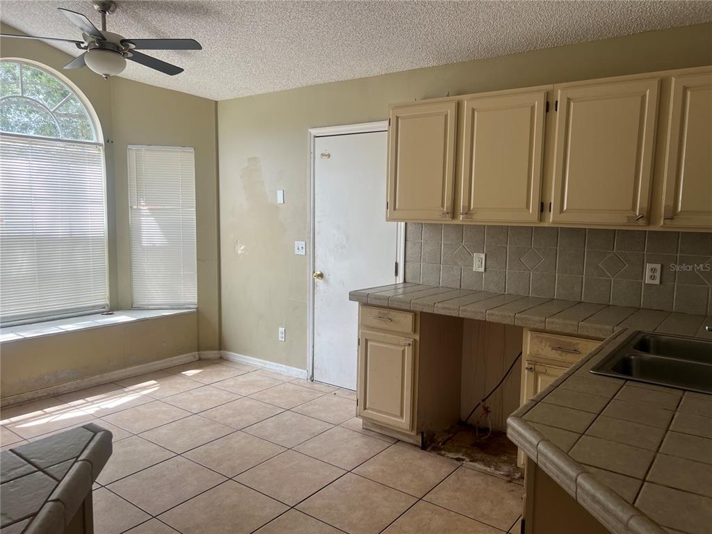 A kitchen with tan tiled countertops, light-colored cabinets, and a windowed dining nook — 1982 GREYSTONE TRAIL, ORLANDO, FL