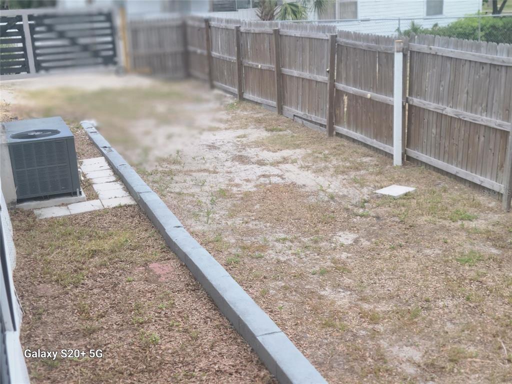 A fenced backyard features a sandy lawn, a concrete border, and an outdoor HVAC unit — 2220 E 17TH AVENUE, TAMPA, FL