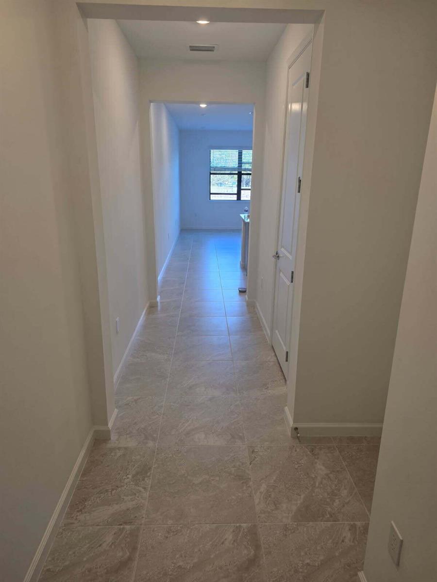 A hallway with light-colored tile flooring leads toward a room with a window — 7783 SW Bentley Lane, Stuart FL 34997, STUART, FL
