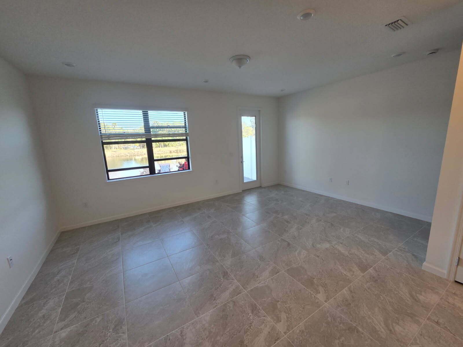 An empty room with light-colored tile flooring, white walls, a window, and a glass door — 7783 SW Bentley Lane, Stuart FL 34997, STUART, FL