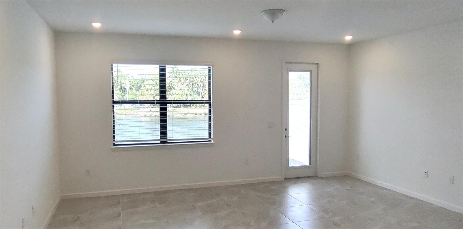 A bright, empty room features white walls, tile flooring, a large window, and a glass door — 7783 SW Bentley Lane, Stuart FL 34997, STUART, FL