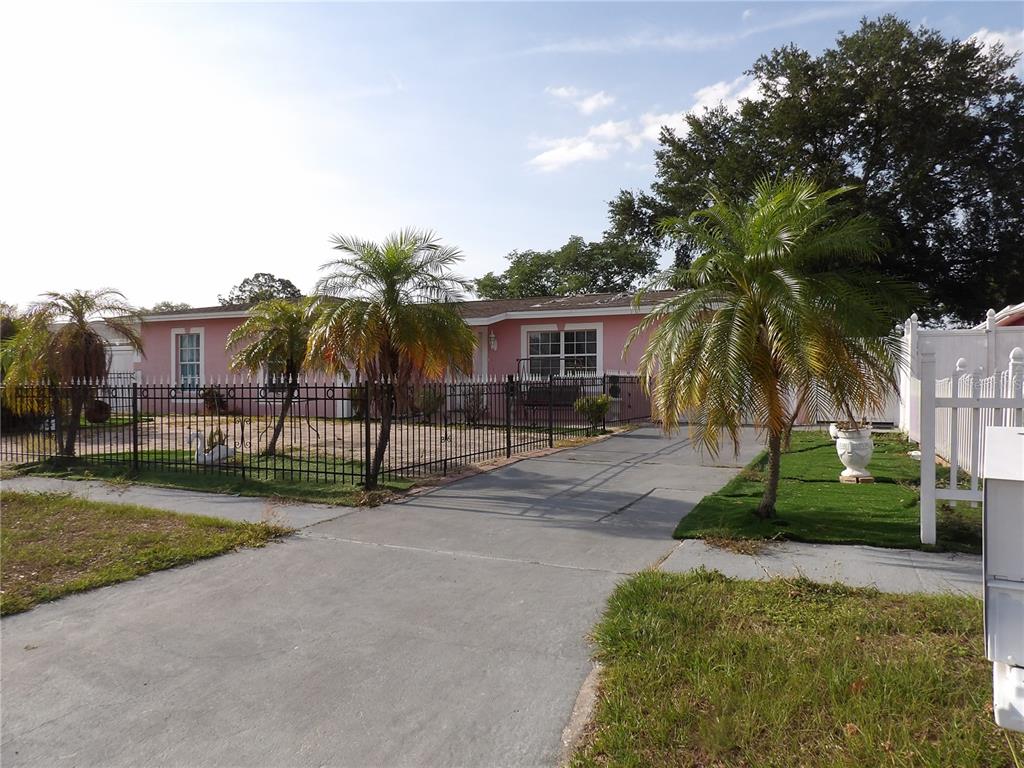 A pink single-story house features a black metal fence and palm trees in the yard — 6521 W HANNA AVENUE, TAMPA, FL