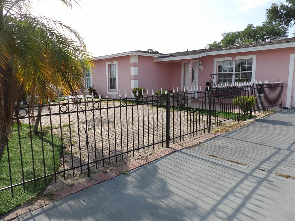 A pink single-story house features a paved front patio enclosed by a black metal fence — 6521 W HANNA AVENUE, TAMPA, FL