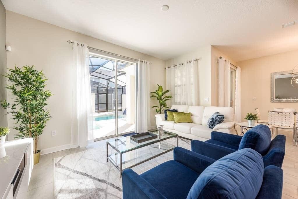 A living room features blue armchairs, a white sofa, a glass coffee table, and pool views — 4814 LOVE STOREY LANE, KISSIMMEE, FL