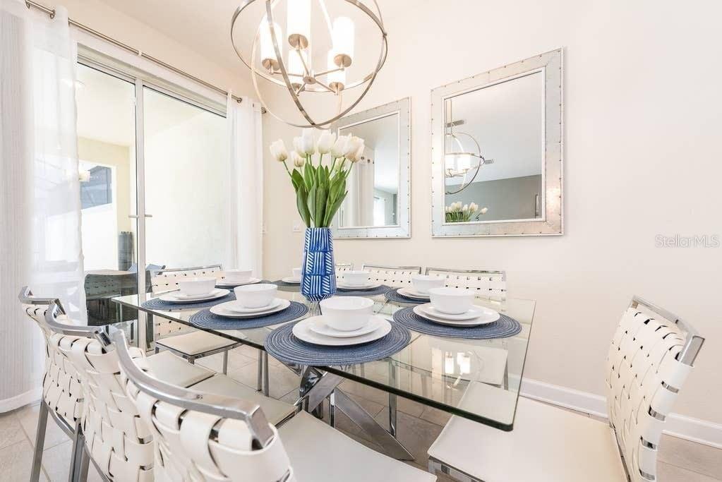 A dining room features a glass-topped table, white chairs, a modern chandelier, and wall mirrors — 4814 LOVE STOREY LANE, KISSIMMEE, FL