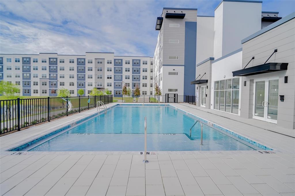 A rectangular swimming pool sits on a paved patio in front of a modern apartment building — 5587 MILLENIA PARK UNIT 201, ORLANDO, FL