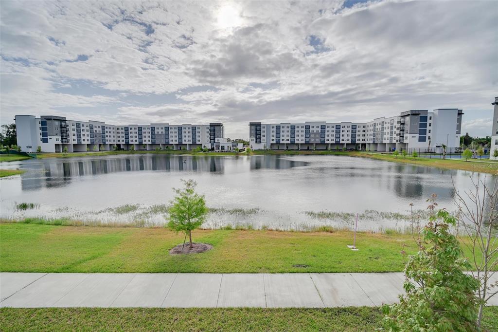 A large pond sits in front of two modern multi-story apartment buildings under a cloudy sky — 5587 MILLENIA PARK UNIT 201, ORLANDO, FL
