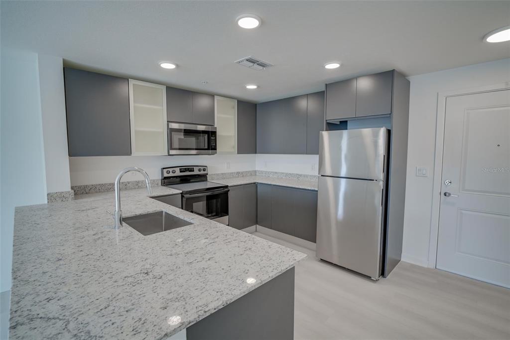 A modern kitchen features gray cabinets, granite countertops, and stainless steel appliances — 5587 MILLENIA PARK UNIT 201, ORLANDO, FL