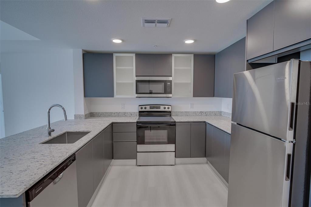 A modern kitchen features gray cabinets, stainless steel appliances, and speckled granite countertops — 5587 MILLENIA PARK UNIT 201, ORLANDO, FL