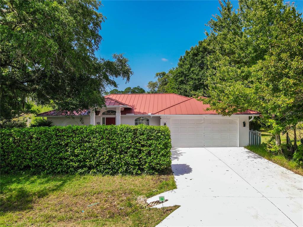 A single-story house with a red metal roof, white garage door, and a manicured hedge — 11 BUNKER HILL DRIVE, PALM COAST, FL