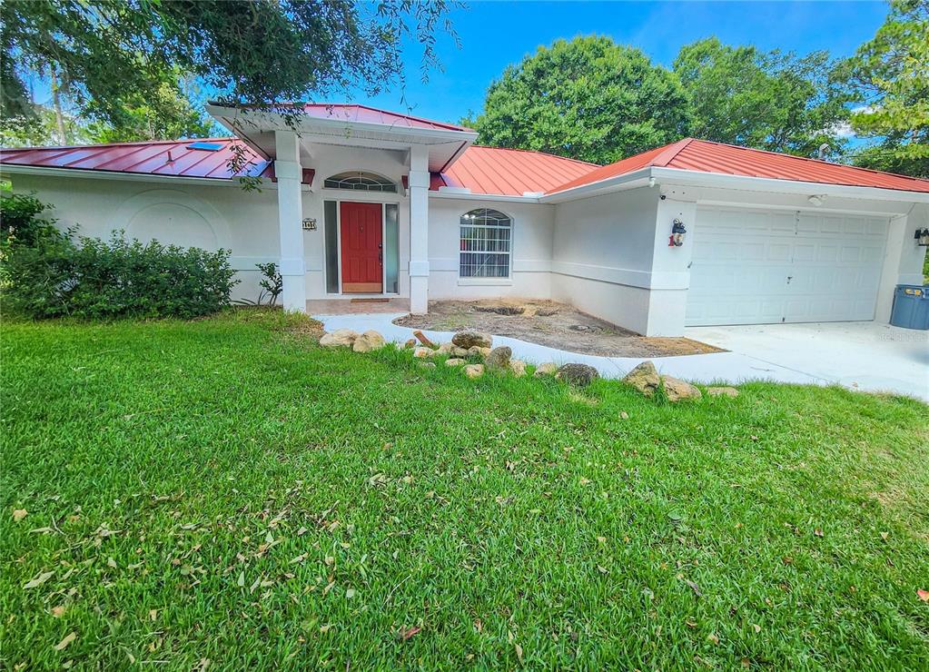 A single-story house with a red metal roof, white stucco exterior, and a red front door — 11 BUNKER HILL DRIVE, PALM COAST, FL